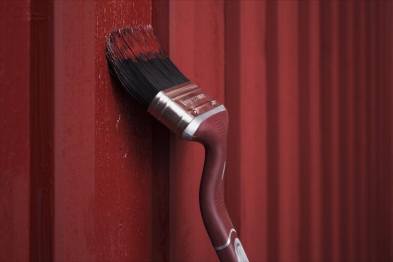 Anza vinklad rödfärgspensel målar med falurödfärg på hus